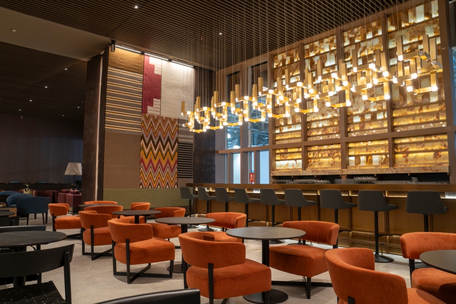 Vue intérieure du salon de signature Latam à Lima avec des meubles modernes, des chaises orange vibrantes et un bar élégant avec un éclairage pendentif.